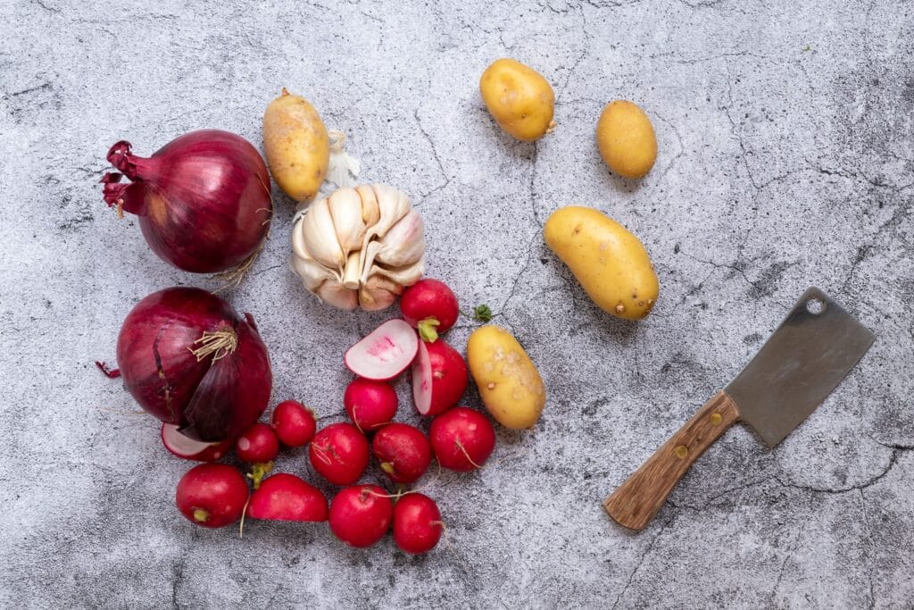 Top view of fresh vegetables and a cleaver on a textured concrete surface, ideal for food photography.