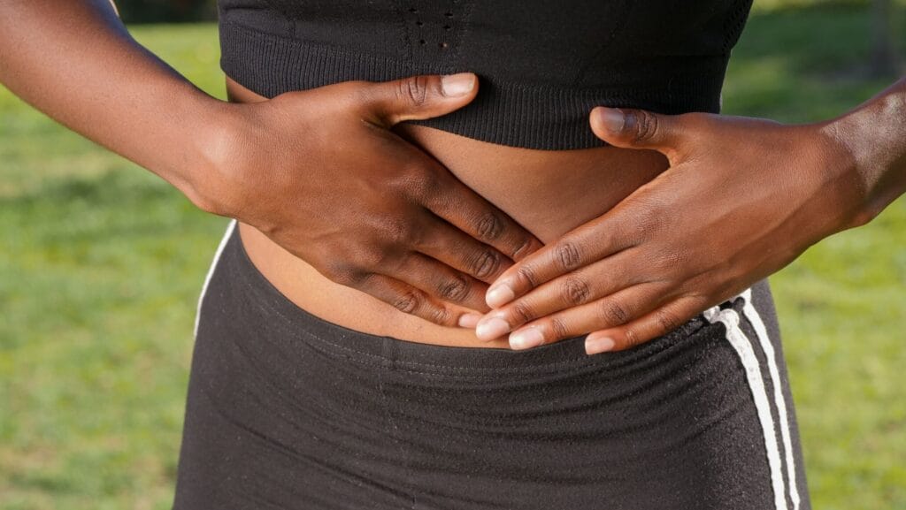 Close-up of a person holding their stomach, indicating abdominal pain outdoors.