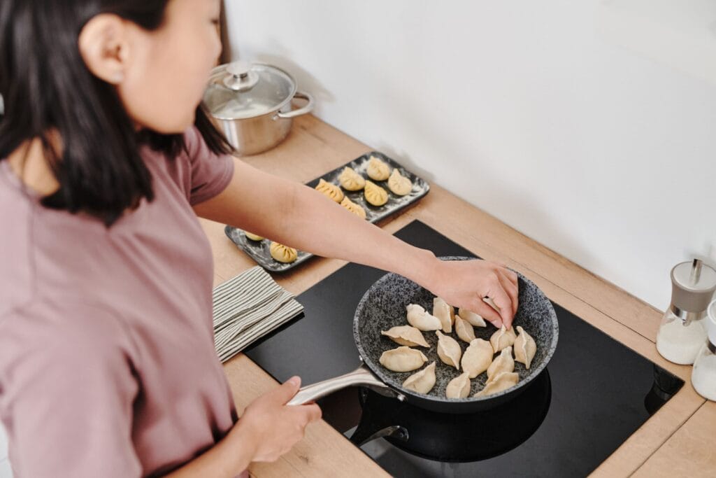 A woman cooking dumplings on a stovetop, showcasing food preparation in a modern kitchen.