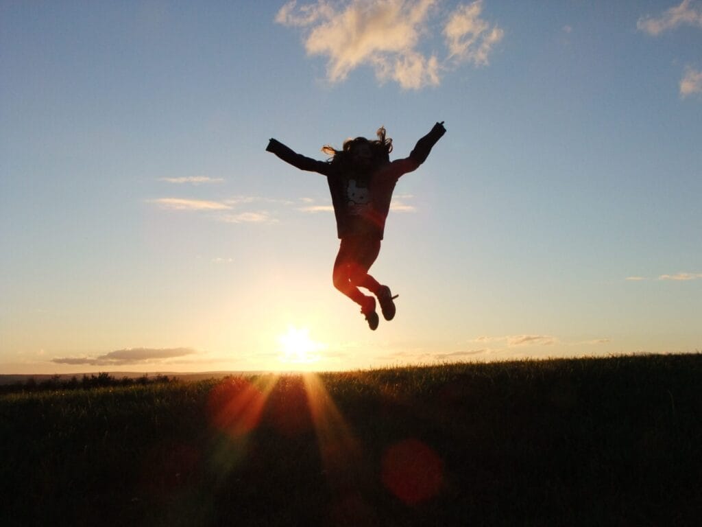Silhouette of a young girl joyfully jumping against a vibrant sunset backdrop.