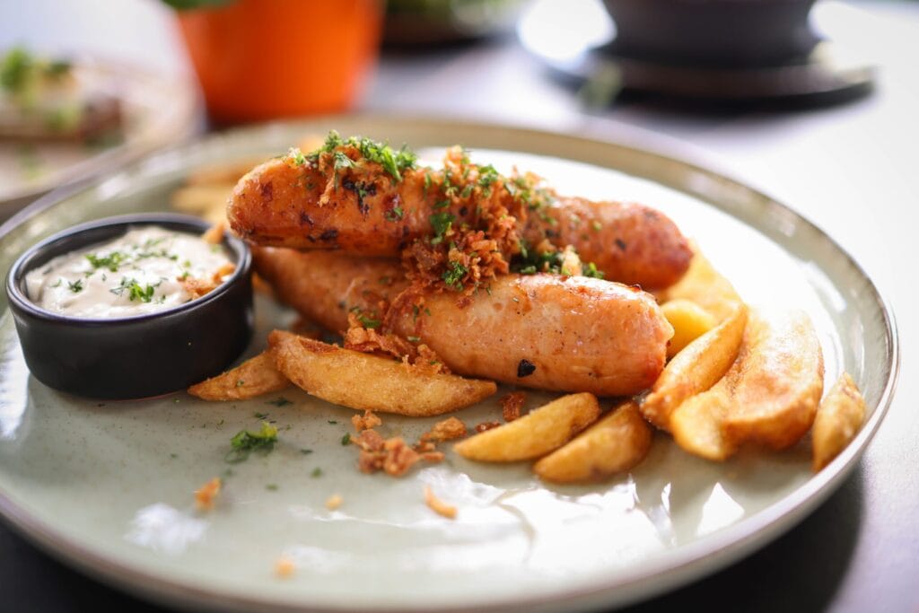 Delicious sausage and crispy french fries served on a plate with a side of dipping sauce.