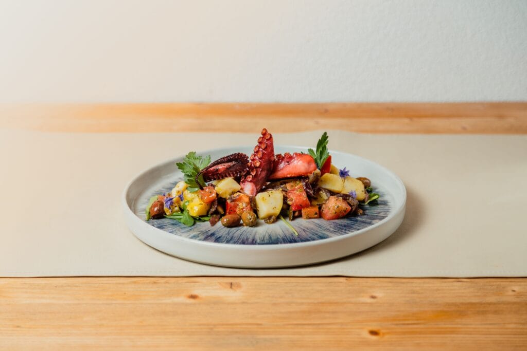 A beautifully plated gourmet octopus dish with colorful mixed vegetables on a decorative plate.