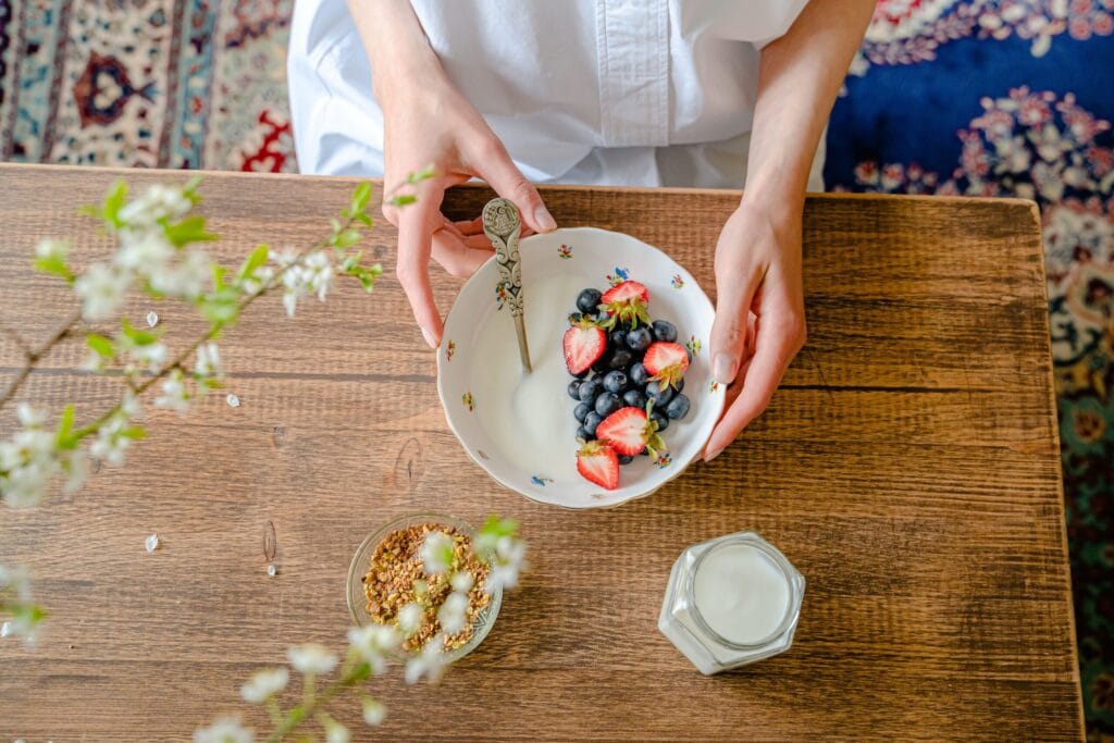 A top view of a person preparing a healthy breakfast with fresh berries, milk, and granola on a wooden table.