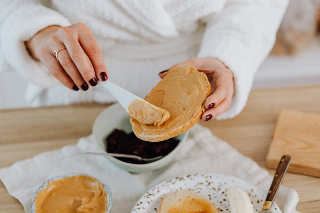 Close-up of a woman spreading creamy peanut butter on toast, perfect for breakfast.